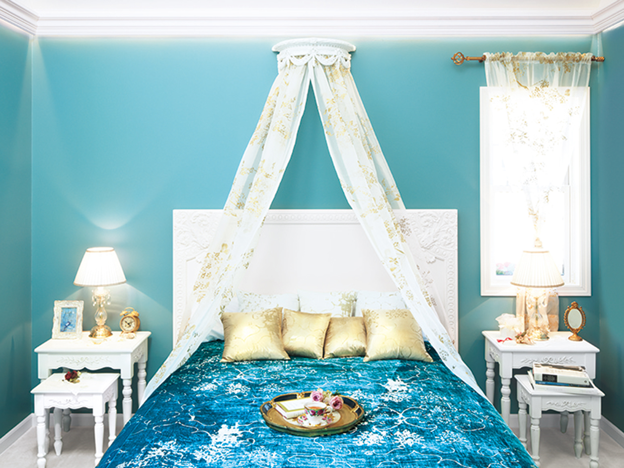 混じりけのない無垢（むく）な白い天井にブルーの壁が映える2階のベッドルーム。天蓋（てんがい）付きのベッドが優雅な雰囲気を醸し出す。